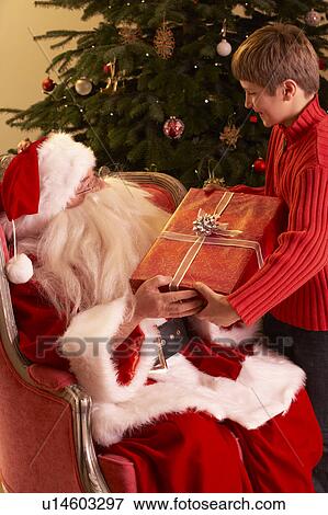 Stock Photo - Santa Claus Giving Gift To Boy In Front Of Christmas Tree. Fotosearch