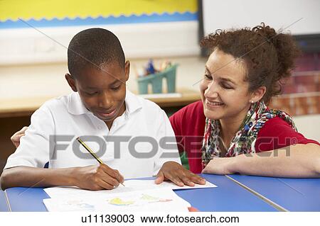 Stock Image - Schoolboy Studying In Classroom With Teacher. Fotosearch