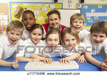 Stock Photograph - Schoolchildren in IT Class Using Computers with teacher. Fotosearch