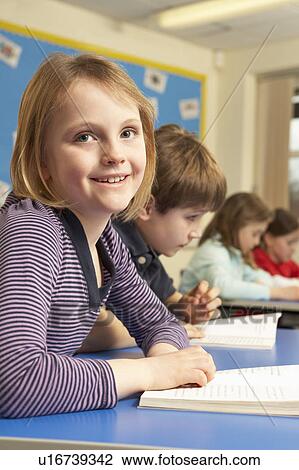 Stock Image - Schoolgirl Reading Book In Classroom. Fotosearch
