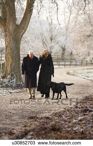 Stock Image - Senior Couple On Winter Walk With Dog Through Frosty Landscape. Fotosearch