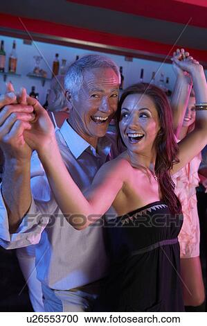 Stock Image - Senior Man Dancing With Younger Woman In Busy Bar. Fotosearch