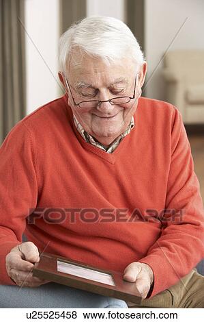 Stock Photo - Senior Man Looking At Photograph In Frame. Fotosearch