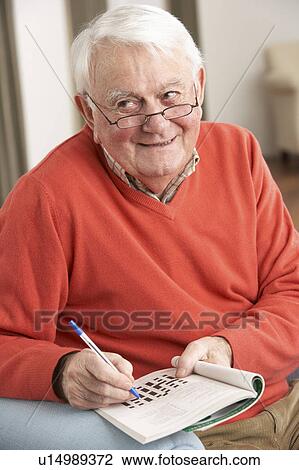 Stock Image - Senior Man Relaxing In Chair At Home Completing Crossword. Fotosearch