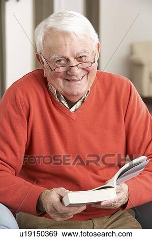 Stock Photo - Senior Man Relaxing In Chair At Home Reading Book. Fotosearch