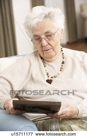 Stock Photo - Senior Woman Looking At Photograph In Frame. Fotosearch