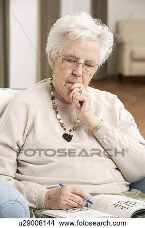 Picture - Senior Woman Relaxing In Chair At Home Completing Crossword. Fotosearch