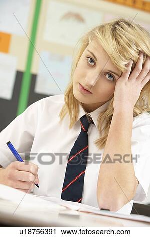 Stock Image - Stressed Female Teenage Student Studying In Classroom. Fotosearch