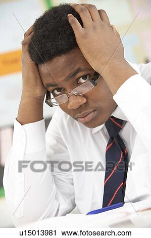 Stock Image - Stressed Male Teenage Student Studying In Classroom. Fotosearch