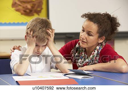 Stock Image - Stressed Schoolboy Studying In Classroom With Teacher. Fotosearch