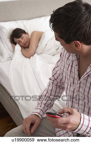 Suspicious Husband Checking Wife's Mobile Phone Whilst She Sleeps View Large Photo Image Stock Photo - Suspicious Husband Checking Wife's Mobile Phone Whilst She Sleeps. Fotosearch