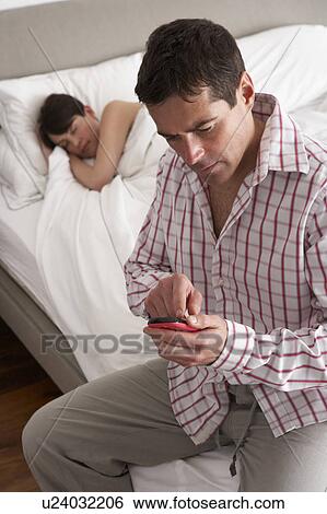 Stock Photograph - Suspicious Husband Checking Wife's Mobile Phone Whilst She Sleeps. Fotosearch