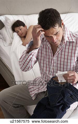 Stock Photography - Suspicious Husband Finding Receipt In Wife's Pocket Whilst She Sleeps. Fotosearch