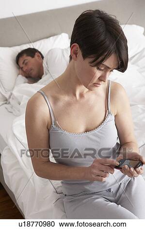 Stock Image - Suspicious Wife Checking Husband's Mobile Phone Whilst He Sleeps. Fotosearch