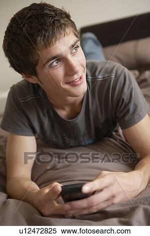 Stock Photography - Teenage Boy Lying In Bedroom Using Mobile Phone. Fotosearch