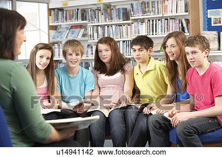 Stock Image - Teenage Students In Library Reading Books With Tutor. Fotosearch