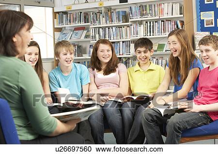 Stock Image - Teenage Students In Library Reading Books With Tutor. Fotosearch