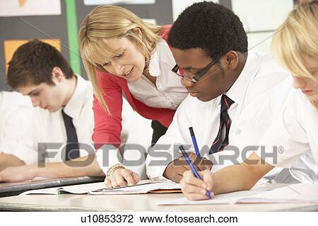 Stock Image - Teenage Students Studying In Classroom With Teacher. Fotosearch