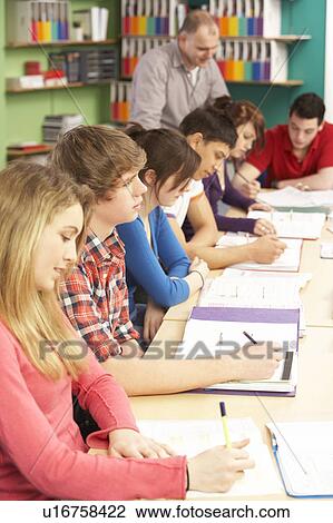 Stock Image - Teenage Students Studying In Classroom With Tutor. Fotosearch