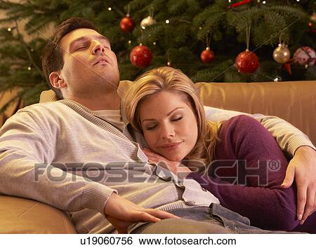 Stock Photograph - Tired Couple Relaxing In Front Of Christmas Tree. Fotosearch