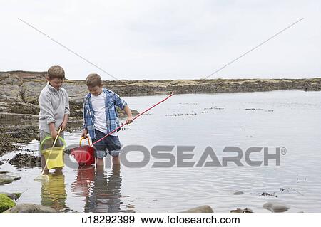 Stock Photo - Two boys collecting shells on beach. Fotosearch
