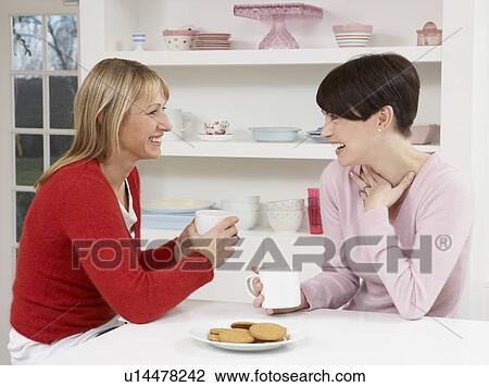 Stock Image - Two Women Enjoying Hot Drink In Kitchen. Fotosearch