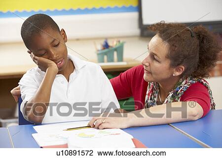 Stock Image - Unhappy Schoolboy Studying In Classroom With Teacher. Fotosearch