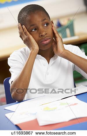 Stock Photo - Unhappy Schoolboy Studying In Classroom. Fotosearch