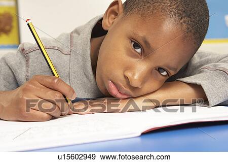 Stock Photo - Unhappy Schoolboy Studying In Classroom. Fotosearch