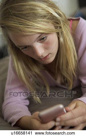 Stock Image - Unhappy Teenage Girl Lying In Bedroom With Mobile Phone. Fotosearch