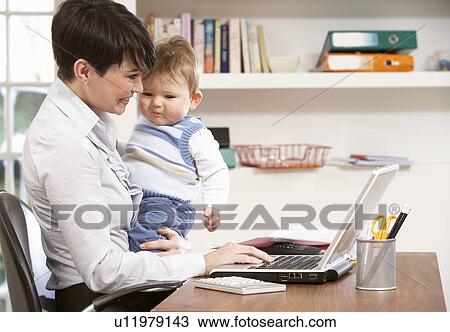 Stock Image - Woman With Baby Working From Home Using Laptop. Fotosearch
