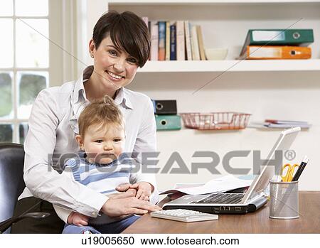 Stock Image - Woman With Baby Working From Home Using Laptop. Fotosearch
