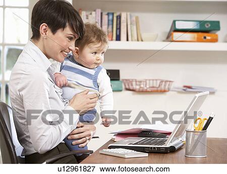 Stock Photo - Woman With Baby Working From Home Using Laptop. Fotosearch