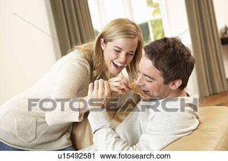 Stock Image - Young couple having fun laughing on sofa. Fotosearch