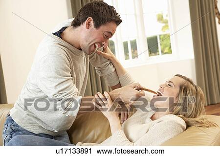 Stock Image - Young couple having fun laughing on sofa. Fotosearch
