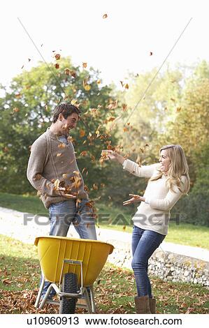 Stock Image - Young couple having fun with autumn leaves in garden. Fotosearch