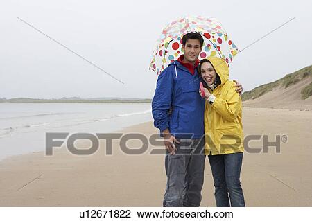Stock Image - Young couple on beach with umbrella. Fotosearch