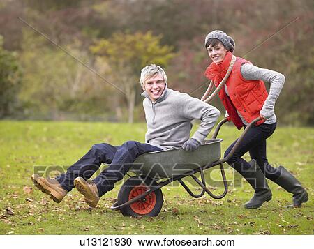 Stock Image - Young couple playing in wheelbarrow. Fotosearch