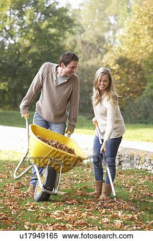 Stock Photography - Young couple raking autumn leaves in garden. Fotosearch
