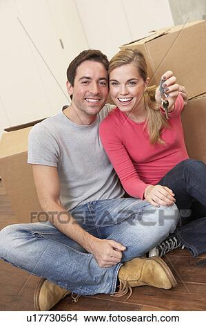 Picture - Young couple sit on the floor around boxes holding key in hand. Fotosearch