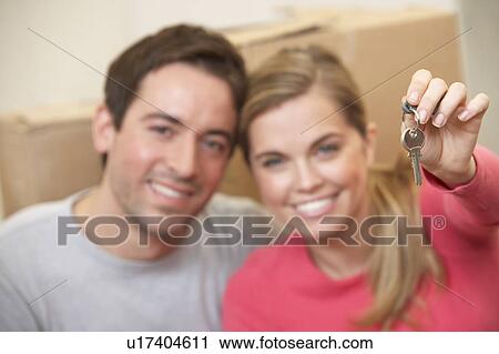 Stock Image - Young couple sit on the floor around boxes holding key in hand. Fotosearch