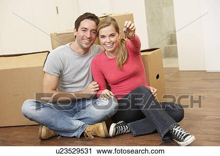 Stock Image - Young couple sit on the floor around boxes holding key in hand. Fotosearch