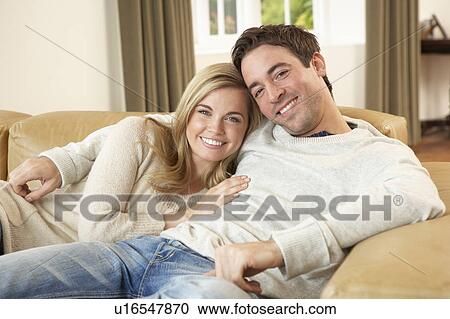 Stock Image - Young couple sitting and relaxing on sofa. Fotosearch