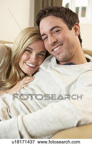Stock Photo - Young couple sitting and relaxing on sofa. Fotosearch