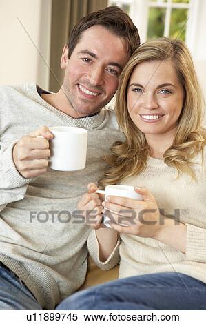 Young couple sitting and relaxing on sofa with cup in hand View Large Photo Image Stock Photography - Young couple sitting and relaxing on sofa with cup in hand. Fotosearch