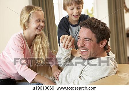 Stock Photo - Young father with children having fun on sofa. Fotosearch