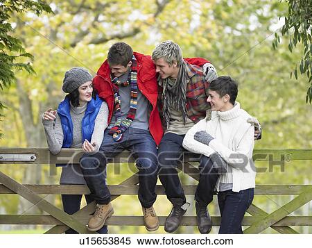 Stock Photography - Young friends sitting on fence. Fotosearch