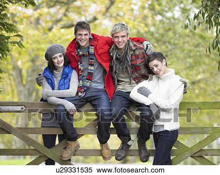 Stock Photography - Young friends sitting on fence. Fotosearch