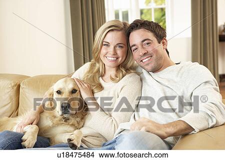 Picture - Young happy couple with dog sitting on sofa. Fotosearch