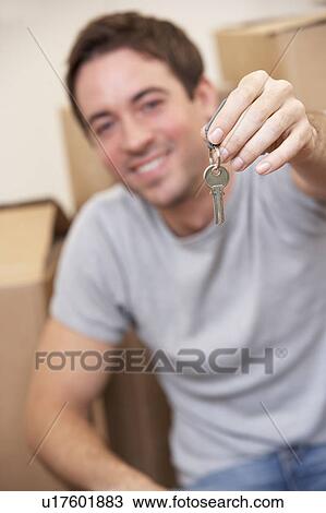 Stock Image - Young man sits on the floor around boxes holding a key in his hand. Fotosearch